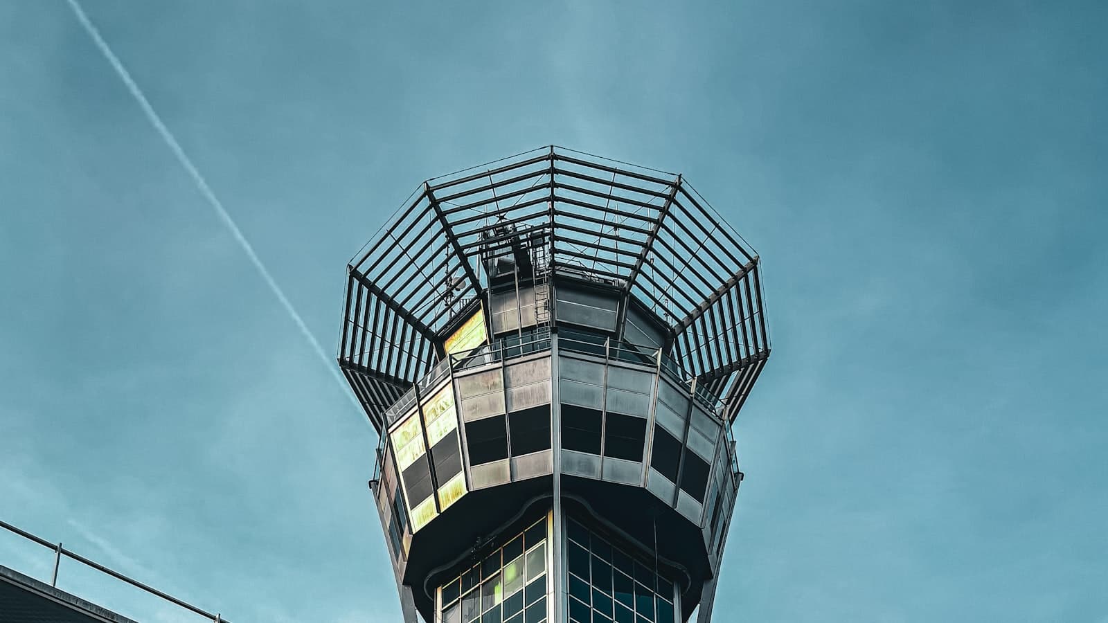 An airport control tower cab against a blue sky, seen from below